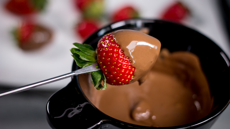 Strawberry on fondue fork, just emerged from dipping into chocolate pot