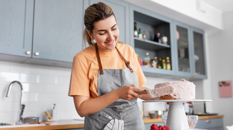 woman frosting a cake in a kitchen