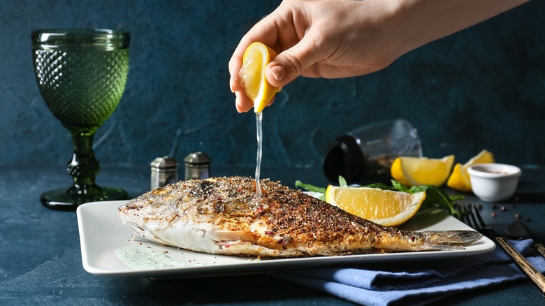 squeezing a lemon on a plate of cooked fish