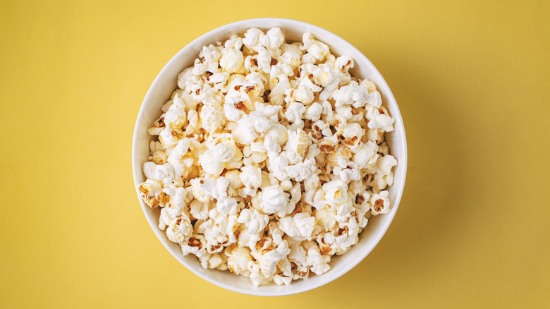 A white bowl of popcorn on yellow background