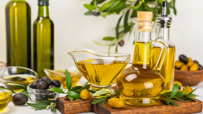 Display of black and green olives with bottles of olive oil on wood cutting board