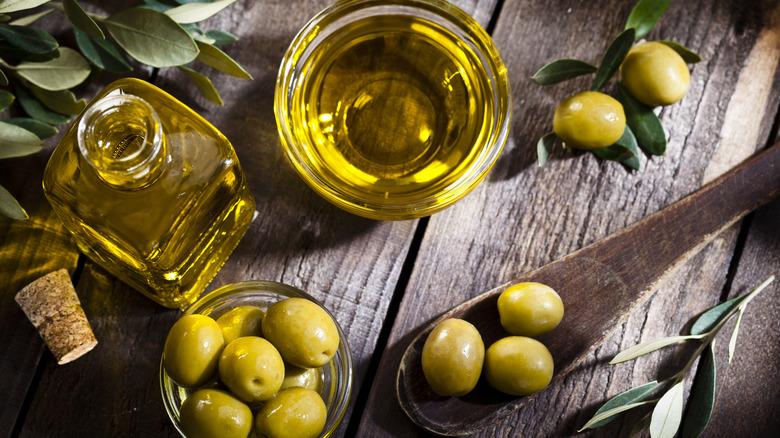 Olives and jars of olive oil with wooden spoon on wooden table viewed from above