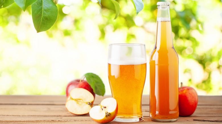 A bottle and glass of hard cider with apples outside