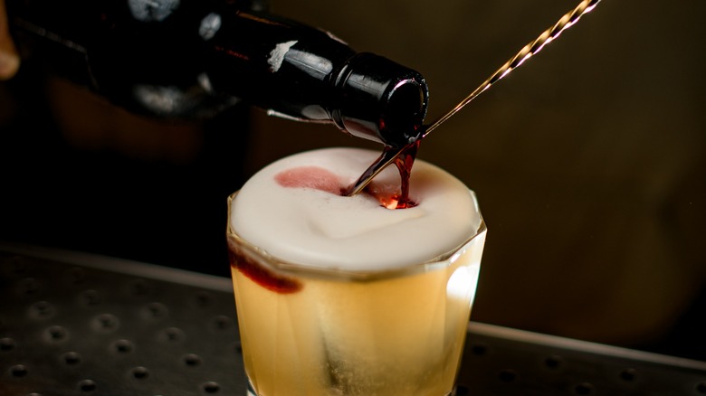 A bottle pouring syrup on top of a spoon in a layered cocktail