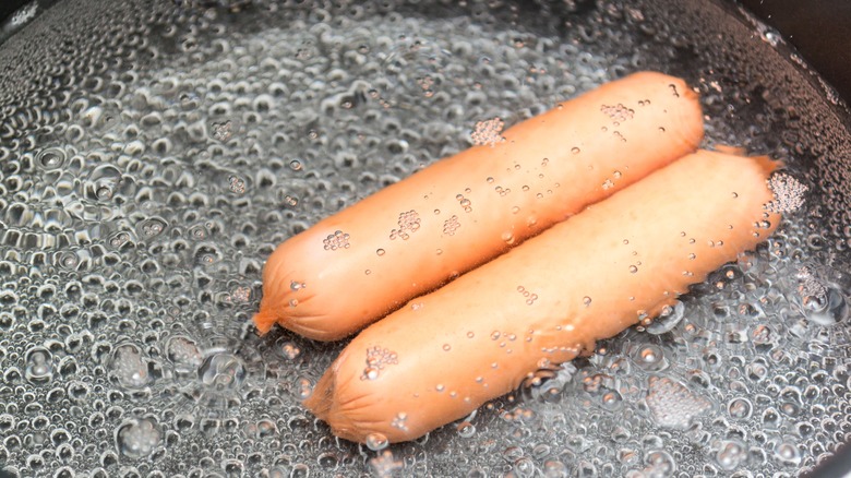 Two hot dogs boiling in water.