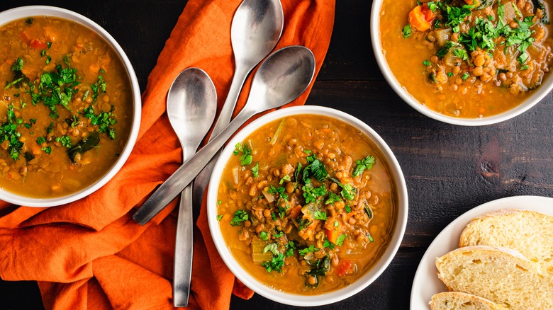 Three bowls of red lentil soup with bread and spoons