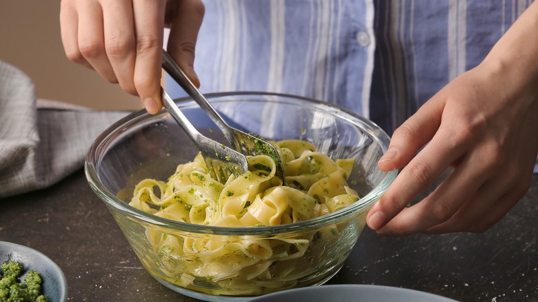 Pasta tongs stirring pesto tagliatelle pasta