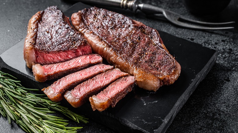 Sliced steak on dark platter with rosemary