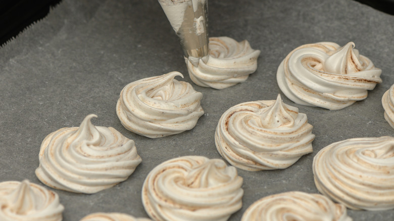 piping meringue cookies onto a lined baking sheet