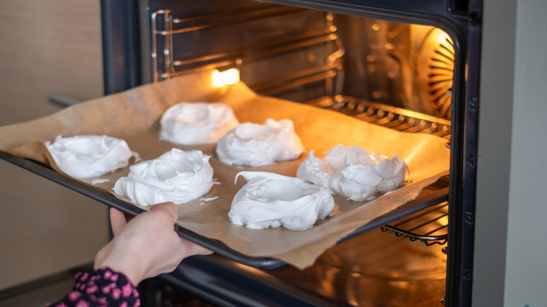 putting meringue cookies into the oven on a baking sheet