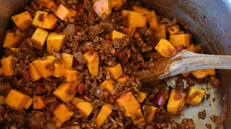 Mixing butternut squash cubes into pan of chilli