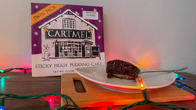 Spoonful of sticky figgy pudding cake on a white plate surrounded by package and Christmas lights