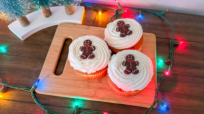 Three vanilla cupcakes topped with chocolate gingerbread men surrounded by Christmas lights