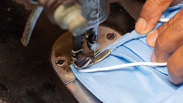 Medical mask under a sewing machine needle being fed threough by hands.