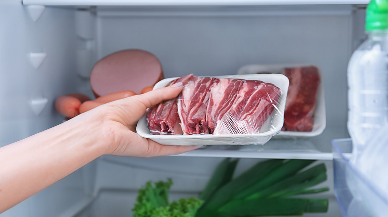 person putting raw meat in refrigerator