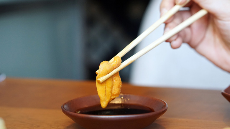 Person dipping raw fish into soy sauce with chopsticks