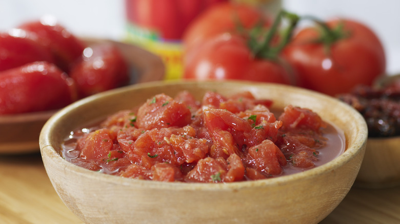 Canned tomatoes in bowl with tomatoes in background