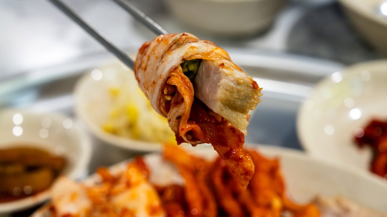 chopsticks holding rolled kimchi and meat