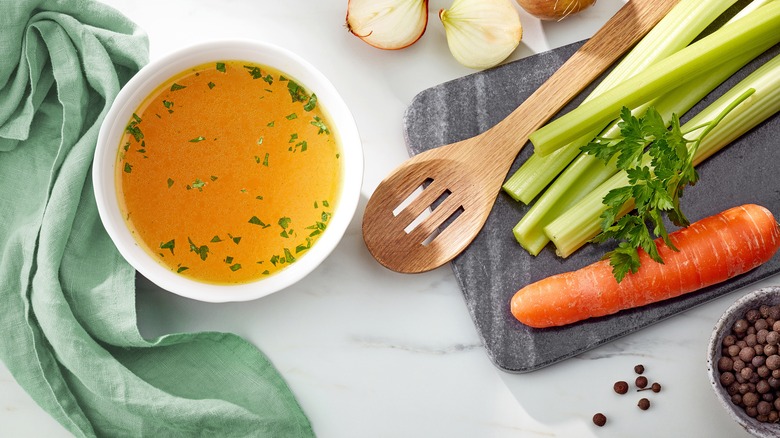 chicken stock next to spoon and vegetables