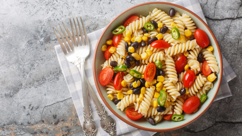 A bowl of pasta salad with tomatoes, corn, black beans, and peppers next to two forks.