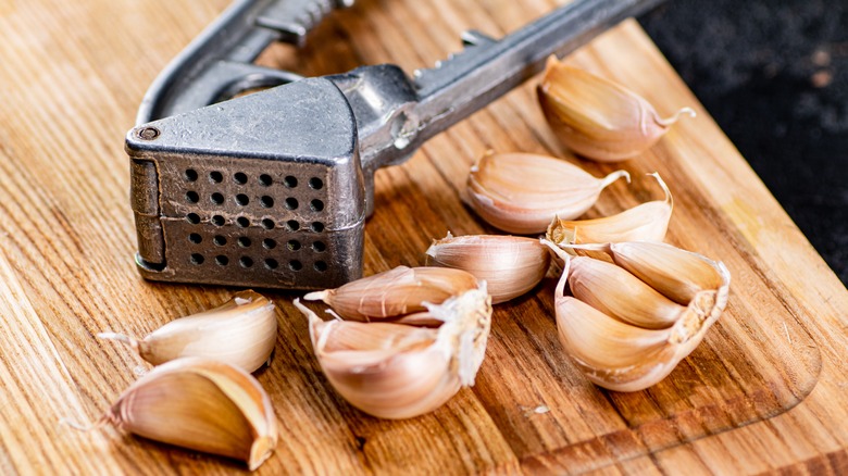 Garlic press with unpeeled garlic cloves on a wood board