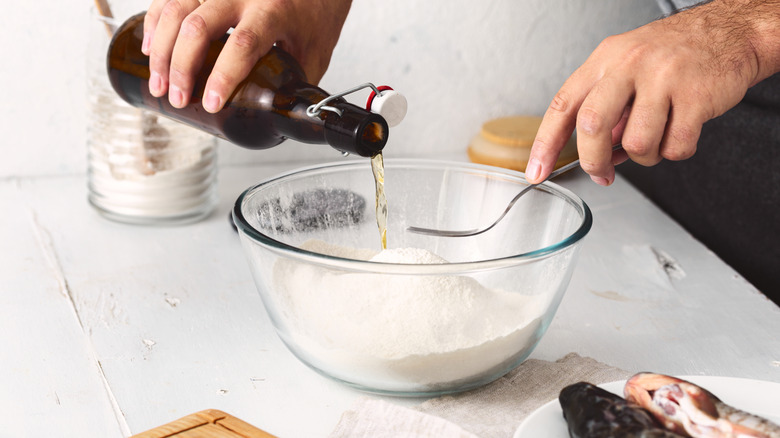 A bottle of beer being poured into a bowl of flour