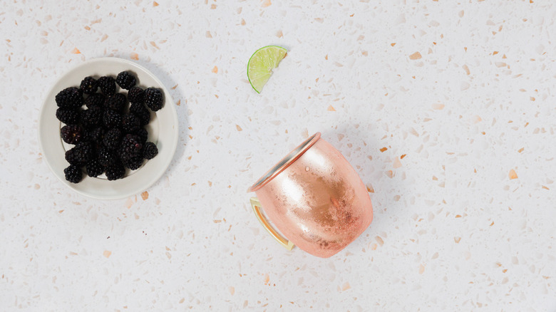 A frosted copper mug next to blackberries and lime