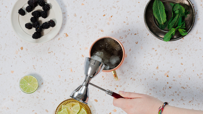 Adding bourbon from a jigger to a copper mule glass