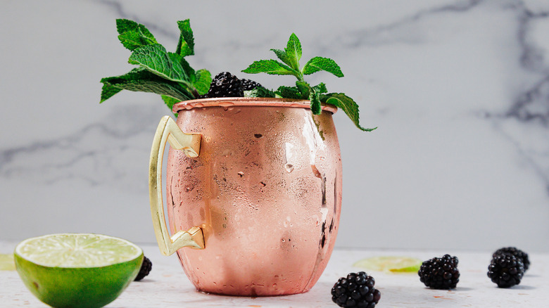 A frosted copper glass of a Kentucky mule with a garnish of mint leaves, blackberries and lime wedges
