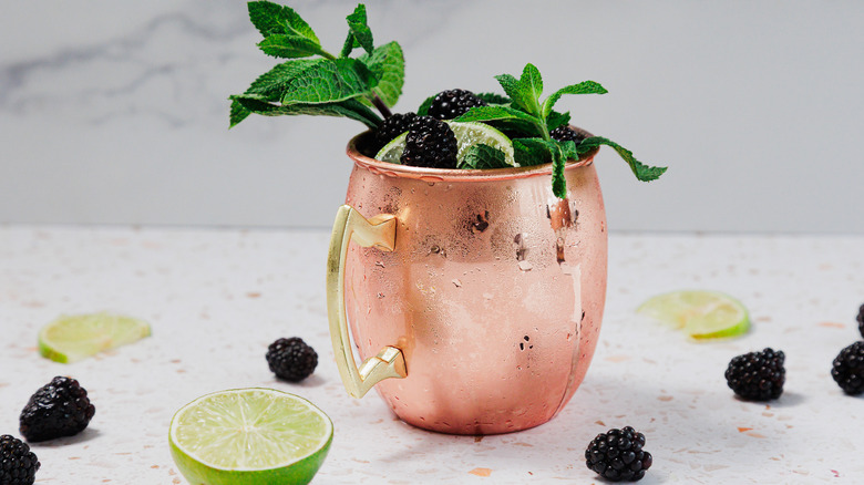 A frosted copper glass of a Kentucky mule with a garnish of mint leaves, blackberries and lime wedges