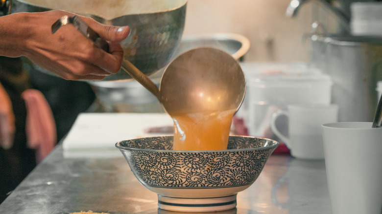 Broth spooned into ramen bowl