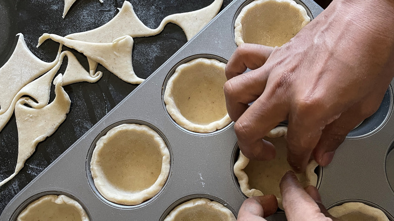 placing pie crust in a muffin tin