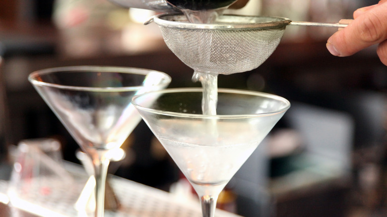 dirty martini being strained into a couple of martini glasses