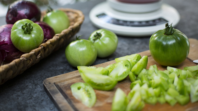 whole and sliced green unripe tomatoes on cutting board