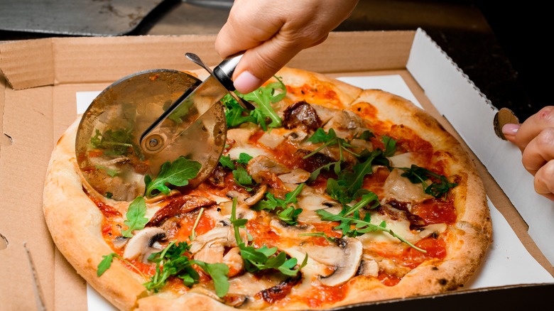 A pizza cutter is used to cut a pizza