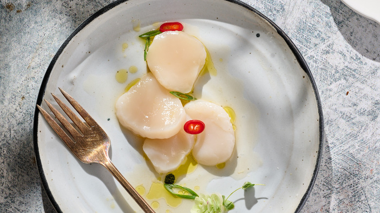 scallop crudo with yuzu, scallions and chile on white plate